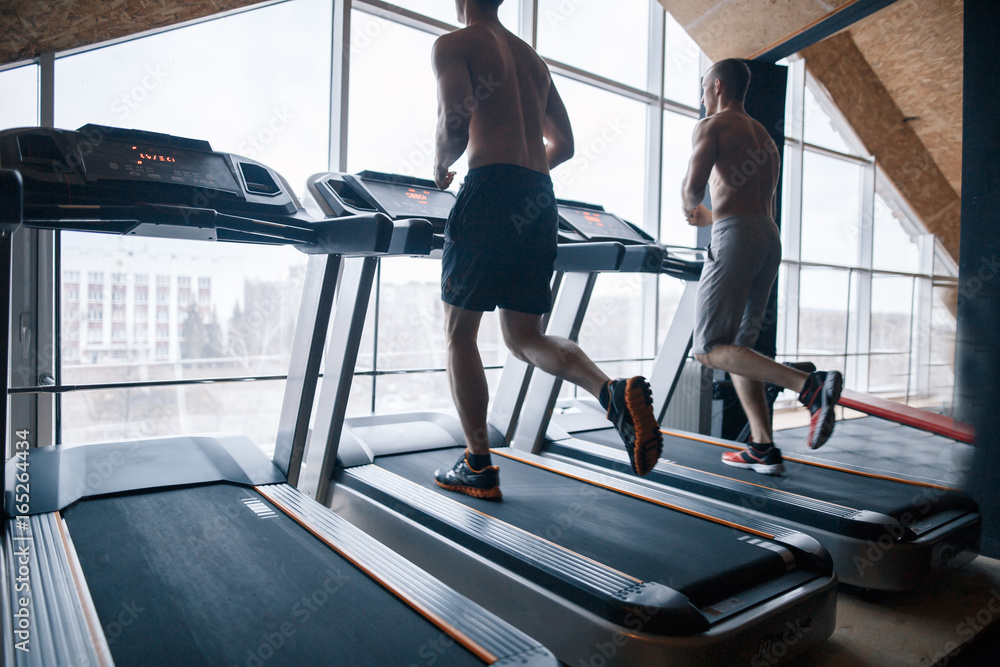 Sport, fitness, lifestyle, technology and people concept - close up of two  men legs walking on treadmills in the gym. Stock Photo