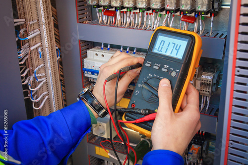 Electrical Engineer adjusts electrical equipment with a multimeter in his hand closeup. photo