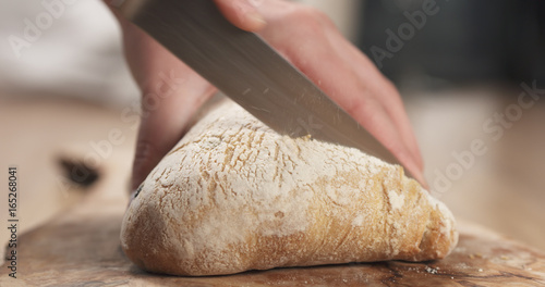 young female hands slicing ciabatta with olives on cutting board