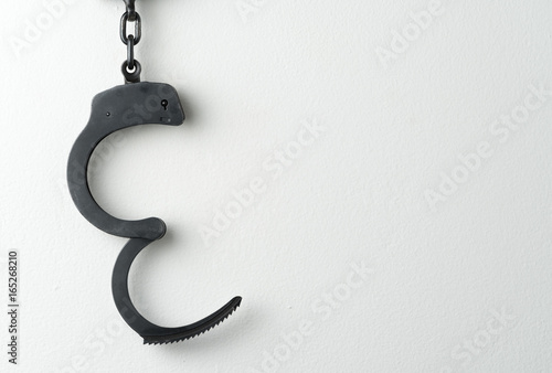 Metal police handcuffs on white painted wall with potential copy space