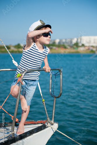 cute little captain kid wearing captain hat and trendy sunglasses peering into the distance standing aboard luxury boat