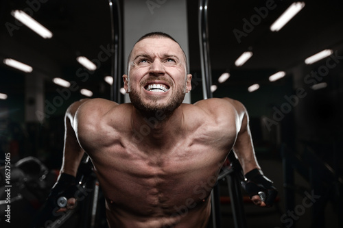 Muscular handsome athletic bodybuilder fitness model posing after exercises in gym on diet . © antondotsenko