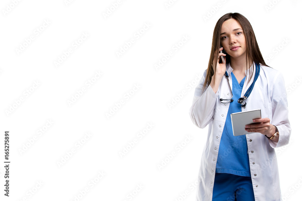 beautiful young woman doctor in a white coat with a stethoscope standing and talking on mobile phone on white background.presenting space for product or text. beautiful young woman doctor in a white coat with a stethoscope standing and talking on mobile phone on white background.presenting space for product or text.