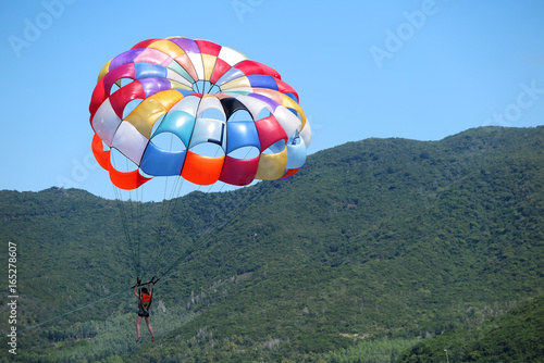 Parasailing girl towing by a boat against a forest island and blue sky photo