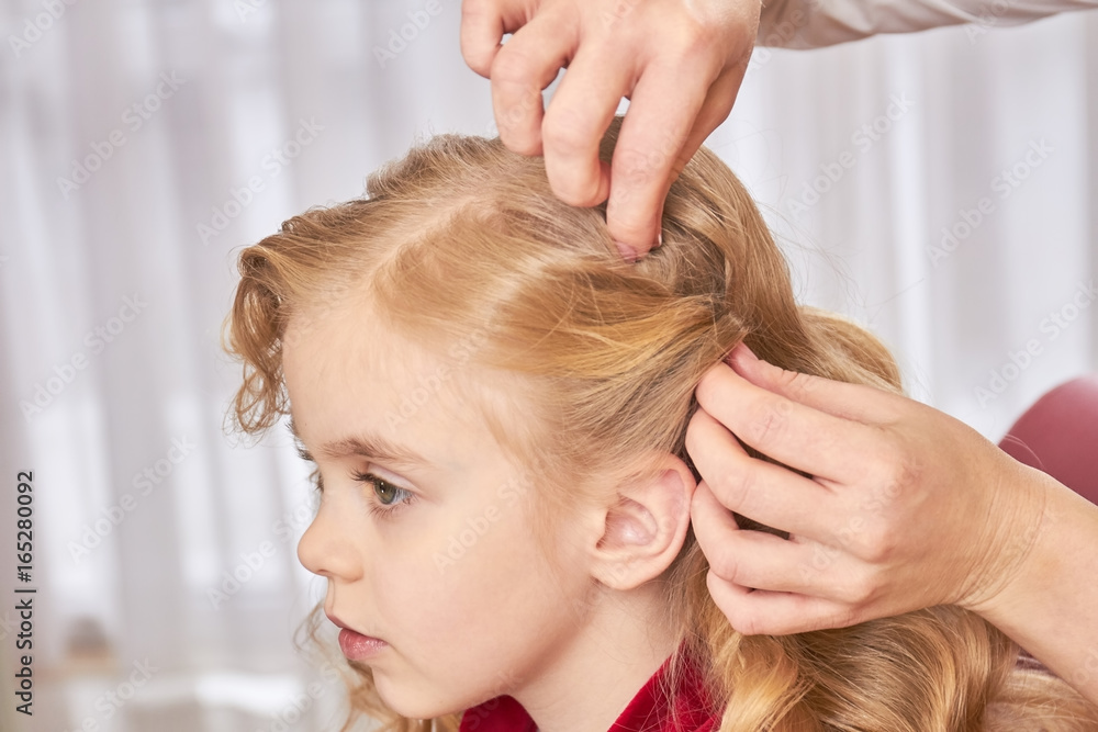 Naklejka premium Little girl, hands of hairdresser. Face of child, side view.