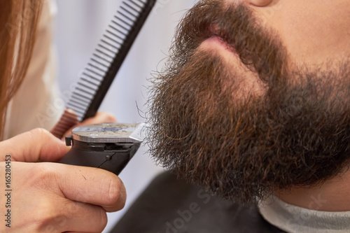Beard trimming close up. Hand of barber with trimmer. How to shape a beard.