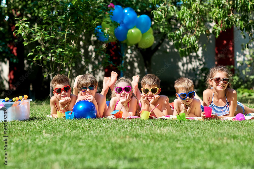 Fototapeta premium Group of children in sunglasses smiling lies on grass in summer.