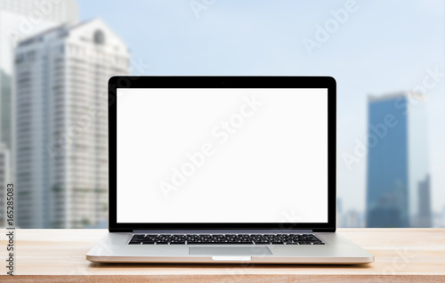 Laptop with blank screen on wood table and town view background. Clipping path include.