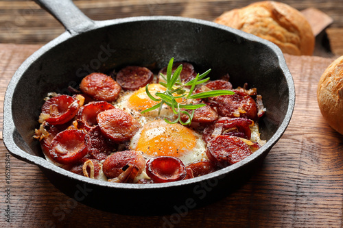 Fried eggs with sausage and onion on frying pan