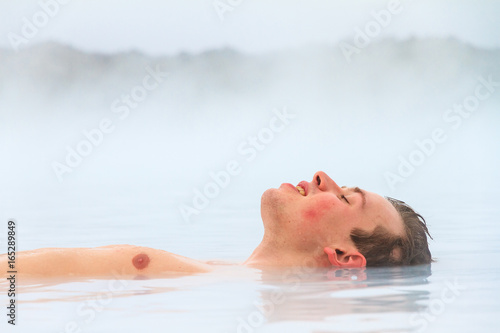 Young man relaxing in blue waters from a hot spring with sulfur and silica in Iceland