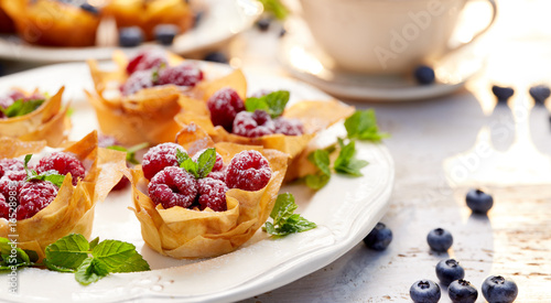 Phyllo cups with Mascarpone cheese filling topped with fresh Raspberries and mint on a white plate, delicious dessert