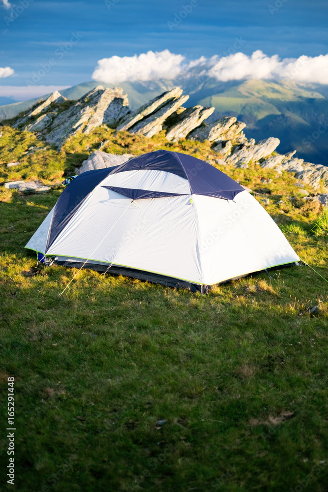 Tourist tent on a grass and next to the rocks. Tent in the mountains. Sunset. Holiday and summer time. Tourist tent on a grass and next to the rocks. Tent in the mountains. Sunset. Holiday and summer time.