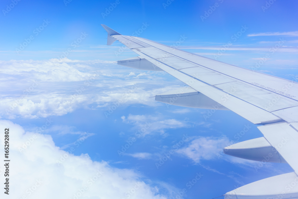 Looking thru airplane 's window seeing wing of airplane , white clouds and blue sky Looking thru airplane 's window seeing wing of airplane , white clouds and blue sky