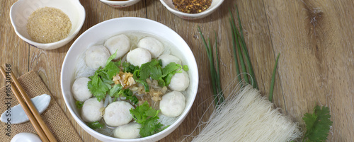 White noodle with pork ball soup in white bowl with seasoning on brown wooden floor thai food / Still Life food, selective focus and space for text.