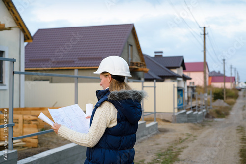 Young female construction specialist reviewing blueprints at construction site