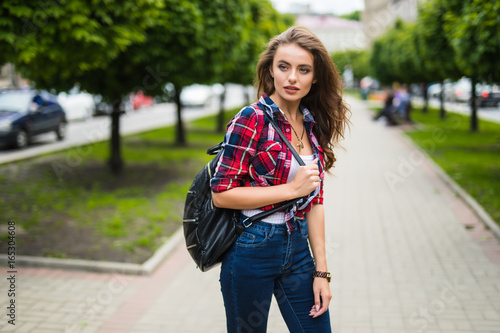 Back view of cheerful attractive young woman with backpack walking in park