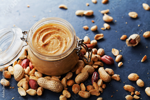 Peanut butter jar and heap of nuts on vintage background.