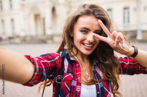 Young girl take selfie from hands with phone with victory sign on summer city street urban life concept