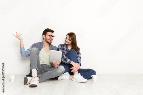 Casual couple discuss something sitting with tablet, studio shot