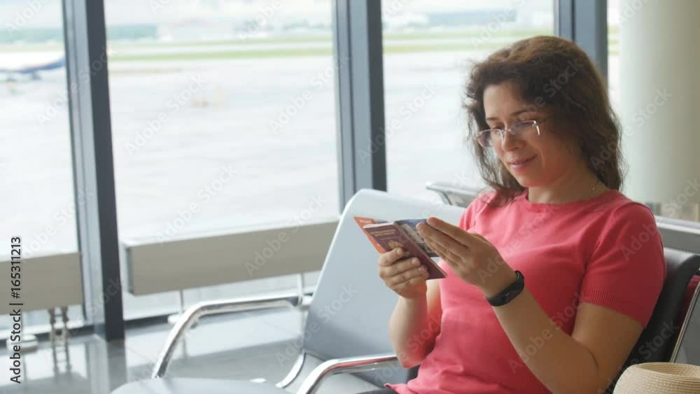 Young female passenger at the airport, using her phone while waiting for her flight Young female passenger at the airport, using her phone while waiting for her flight