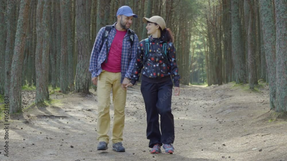 Sports family travels through  forest. A young couple of  tourist with a backpack walk through a forest road. Family travel together, hiking outdoors on nature. Enjoying Nature at Camping.