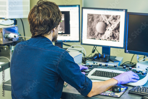 Fotografie Scientist works at a electron microscope control pannel with two monitors in fro