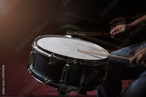 The man is playing drum set in low light background.