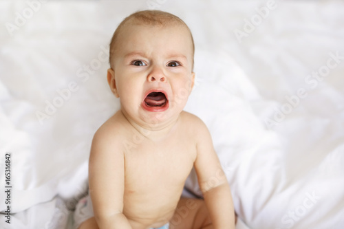 Cute nice little baby girl crying lying with her mom on bed at home.