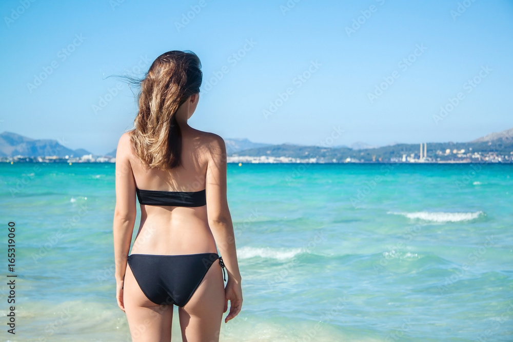 Young woman in bikini with her hand over head enjoying hot summer day on the beautiful Playa de Muro beach, Mallorca, Spain