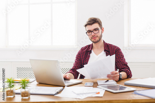Young concentrated businessman using laptop in modern white office