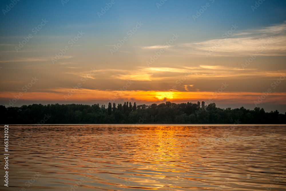 beautiful majestic sunset on the background of the river bank with some unrecognizable swimming people in Kiev Ukraine