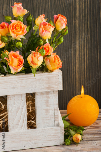 Fresh orange rose flowers in rustic box and lit candle