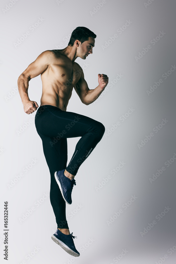Muscle male model in black treand sportswear jumping on white texture background. Studio shoot.