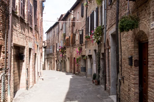Obraz Wąska ulica wioski Umbrii i Toskanii, z drewnianymi drzwiami i doniczkami na ścianach fasad starożytnych murowanych domów