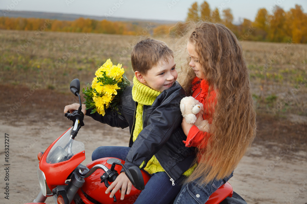 Portrait of a boy with a girl sitting on a toy motorcycle. The boy looks back at his beautiful girlfriend
