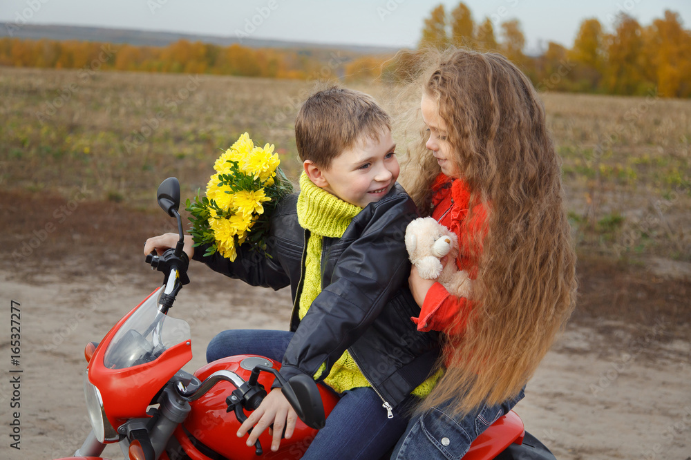 Portrait of a boy with a girl sitting on a toy motorcycle. The boy