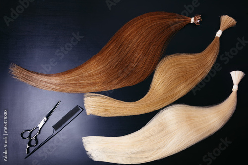 hair extensions of three colors on a dark background with Scissors and comb. copyspace top view. photo