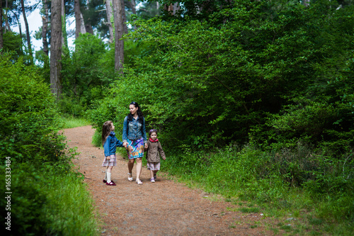mom and two daughters walking along the path through the forest © Nikita