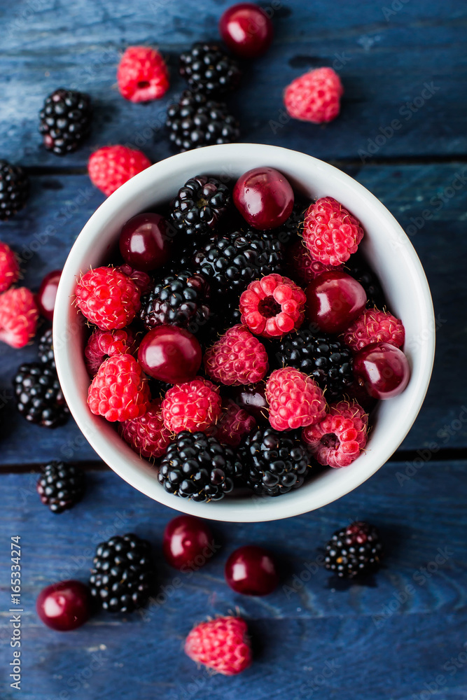 Top view of white cup with Summer fresh berries on blue wooden table background. Copy space. Vegetarian food - raspberry, blackberry and cherry. Rustic style Top view of white cup with Summer fresh berries on blue wooden table background. Copy space. Vegetarian food - raspberry, blackberry and cherry. Rustic style
