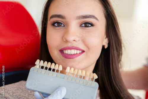 Selection of the color of teeth for a beautiful girl in dentistry.