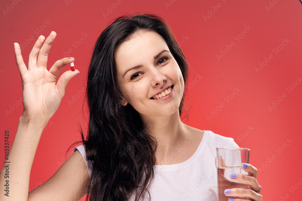 Beautiful young woman on a red background holds a pill Beautiful young woman on a red background holds a pill