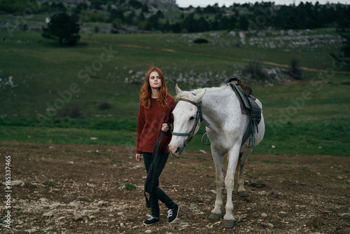 Beautiful young woman in the mountains outdoors walking with a horse