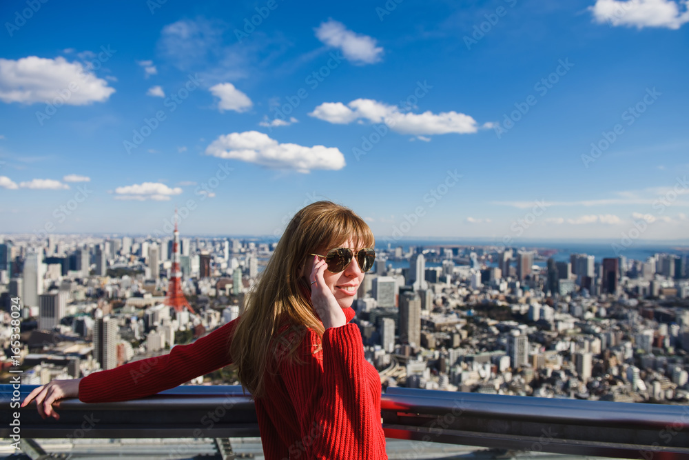Happy young woman looking at Tokyo from rooftops. Girl stands with her back. Tokyo Tower with skyline on background.