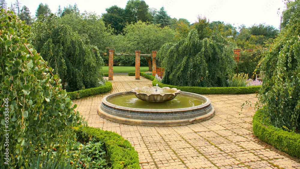 Water fountain in a walled garden with green trees