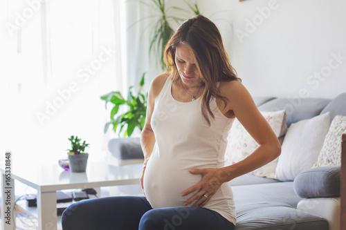 Young pregnant woman, having painful contraction, starting labor photo