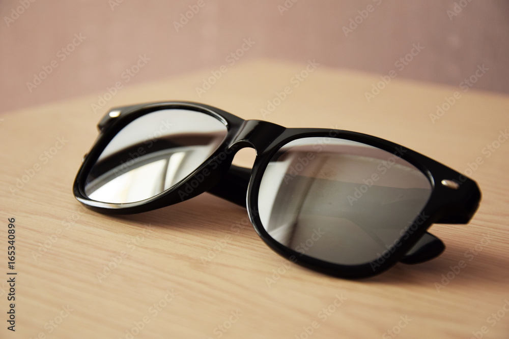Cool sunglasses with black plastic frame isolated on wood background, front view.. Cool sunglasses with black plastic frame isolated on wood background, front view..