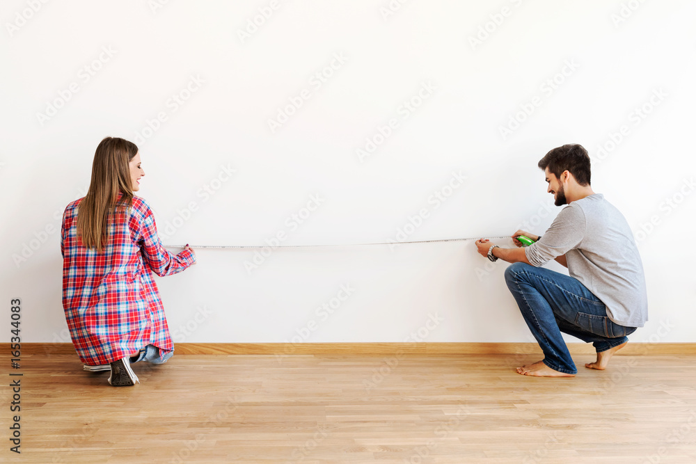 Couple in empty apartment measuring walls - obrazy, fototapety, plakaty 