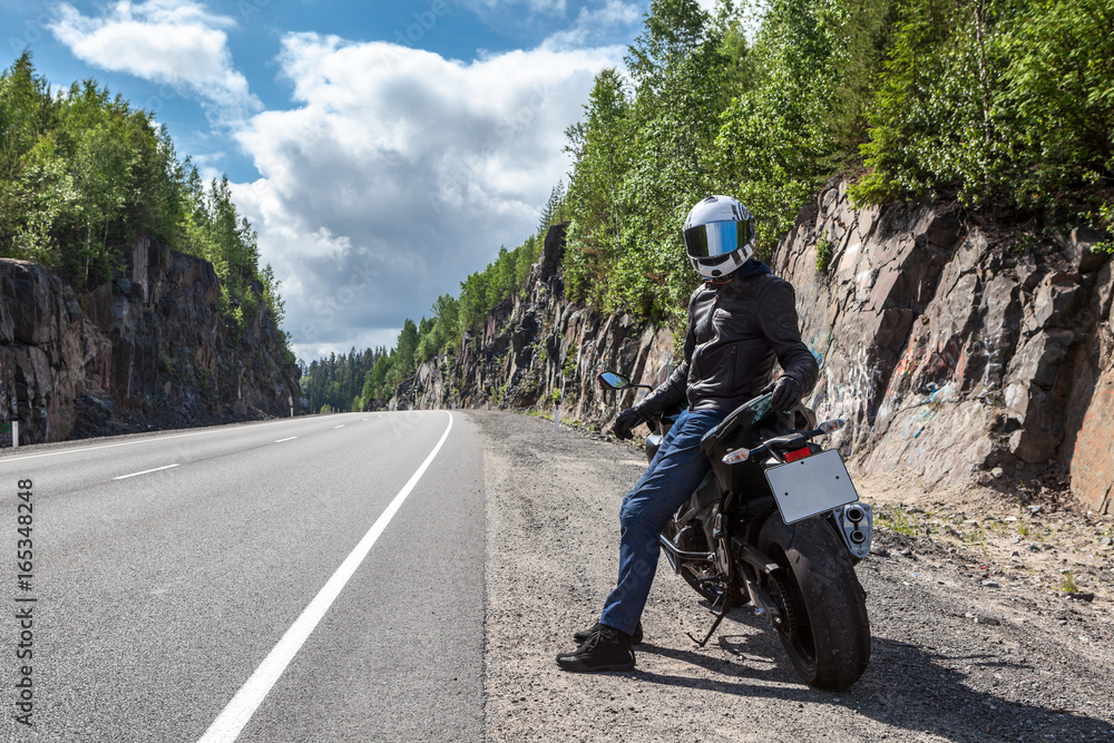 One motortraveler with own motorbike resting on roadside on the mountain asphalt road One motortraveler with own motorbike resting on roadside on the mountain asphalt road