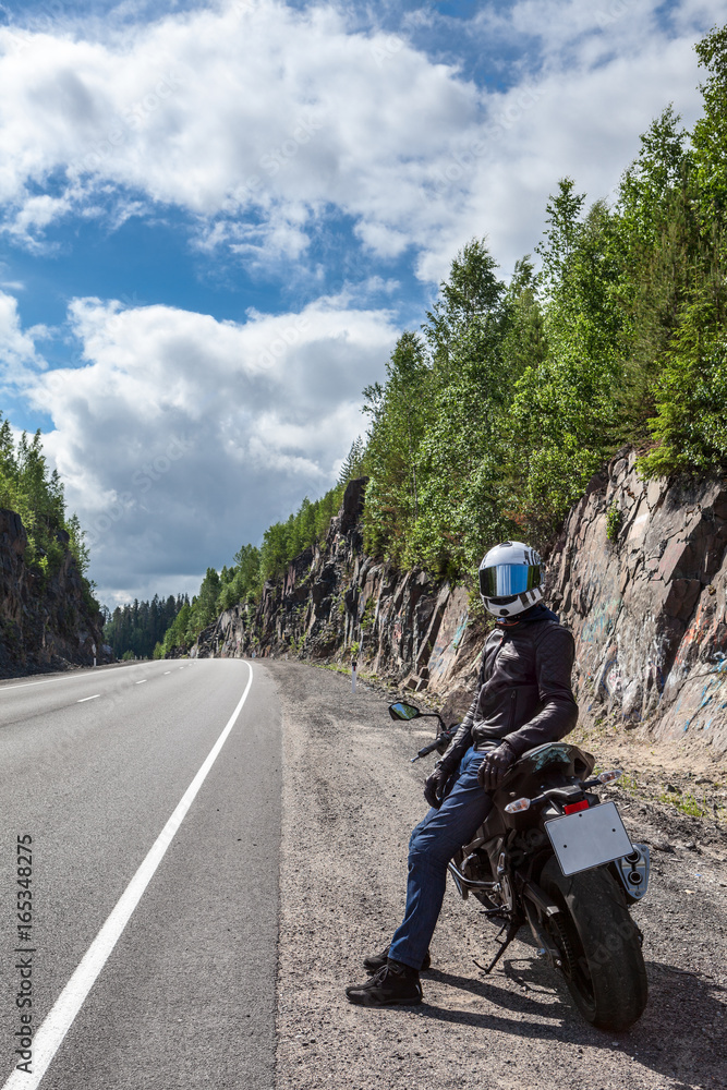 Motorcycle driver resting on roadside on the mountain asphalt road at sunny day Motorcycle driver resting on roadside on the mountain asphalt road at sunny day