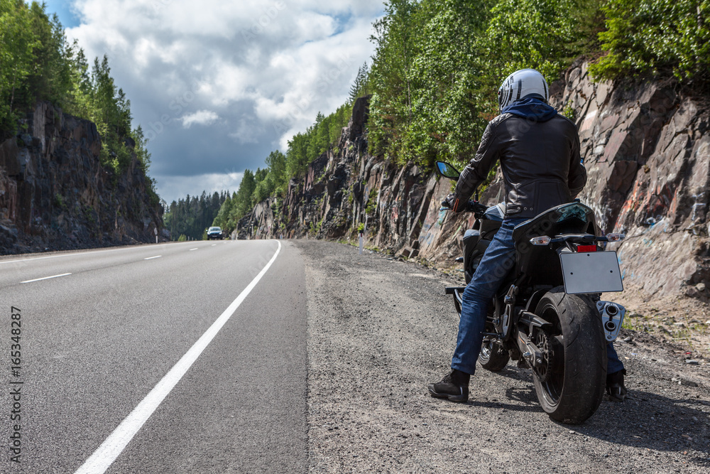 Fototapeta premium Człowiek z nowoczesny motocykl nagi stojący na poboczu drogi asfaltowej góry, widok z tyłu, lato